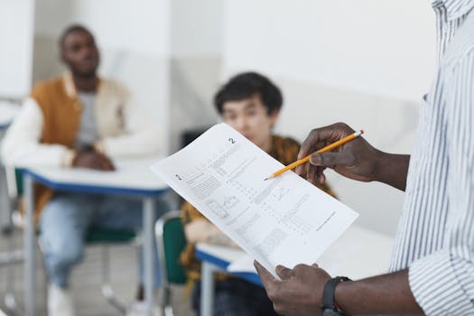 Students working on an exam with a teacher overseeing in a classroom.
